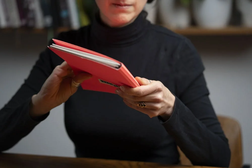 Nahaufnahme einer Frau in schwarzem T-Shirt, die ein rotes Notizbuch hält.
