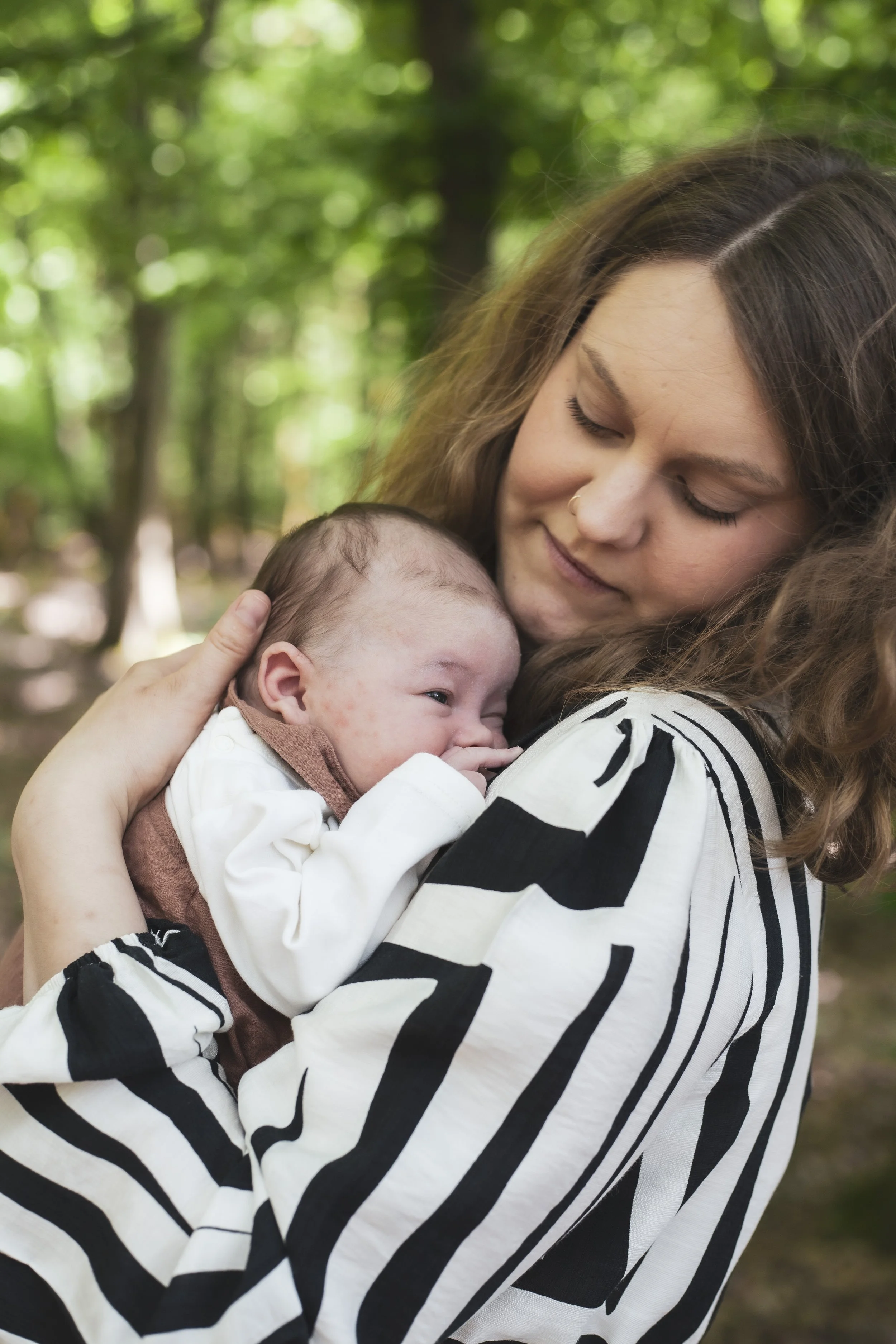 Eine junge Frau hält ein schlafendes Baby in den Armen in einem grünen, bewaldeten Park.