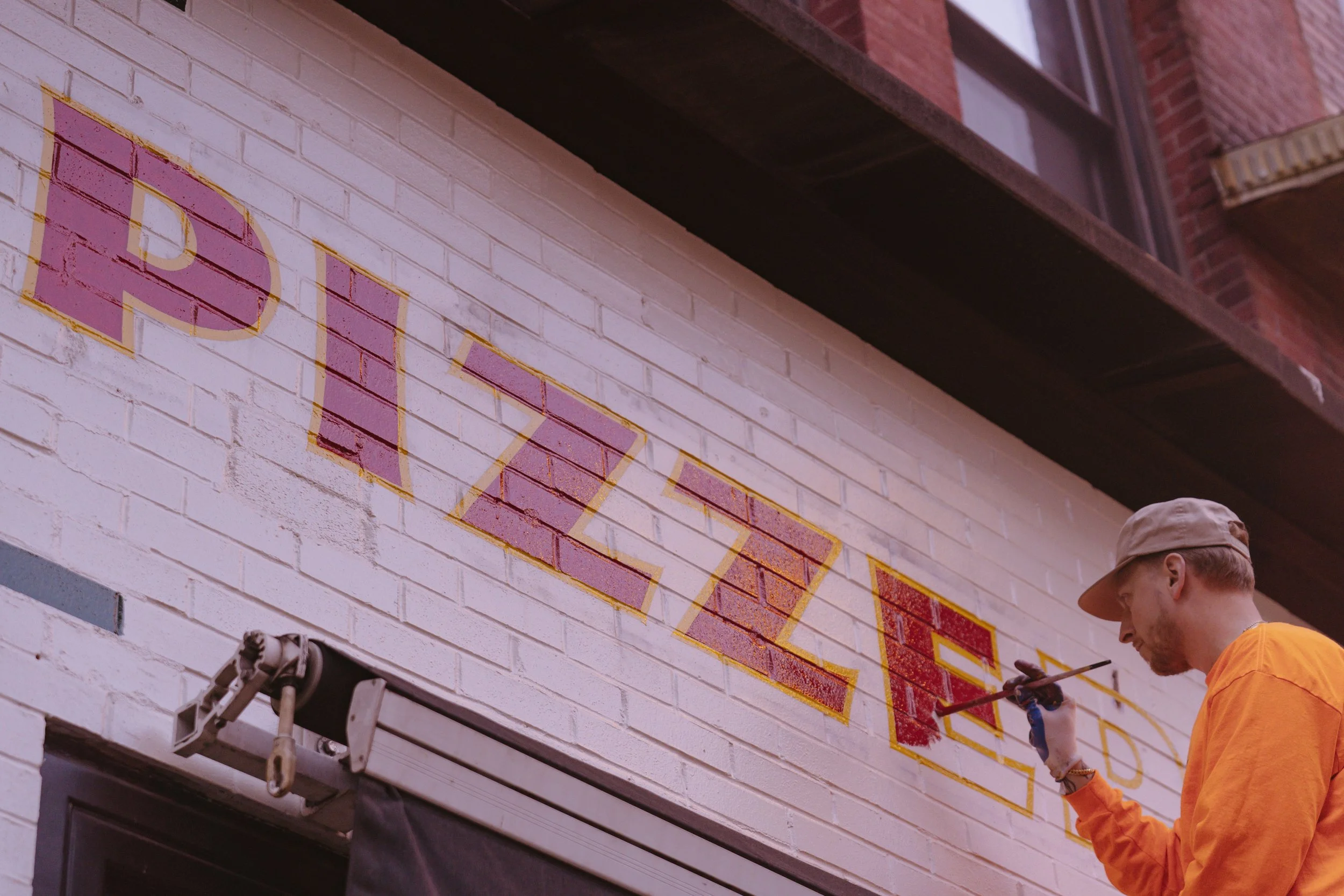 Doug Aldrich hand painting a wall sign for L'industrie Pizzeria in NYC.
