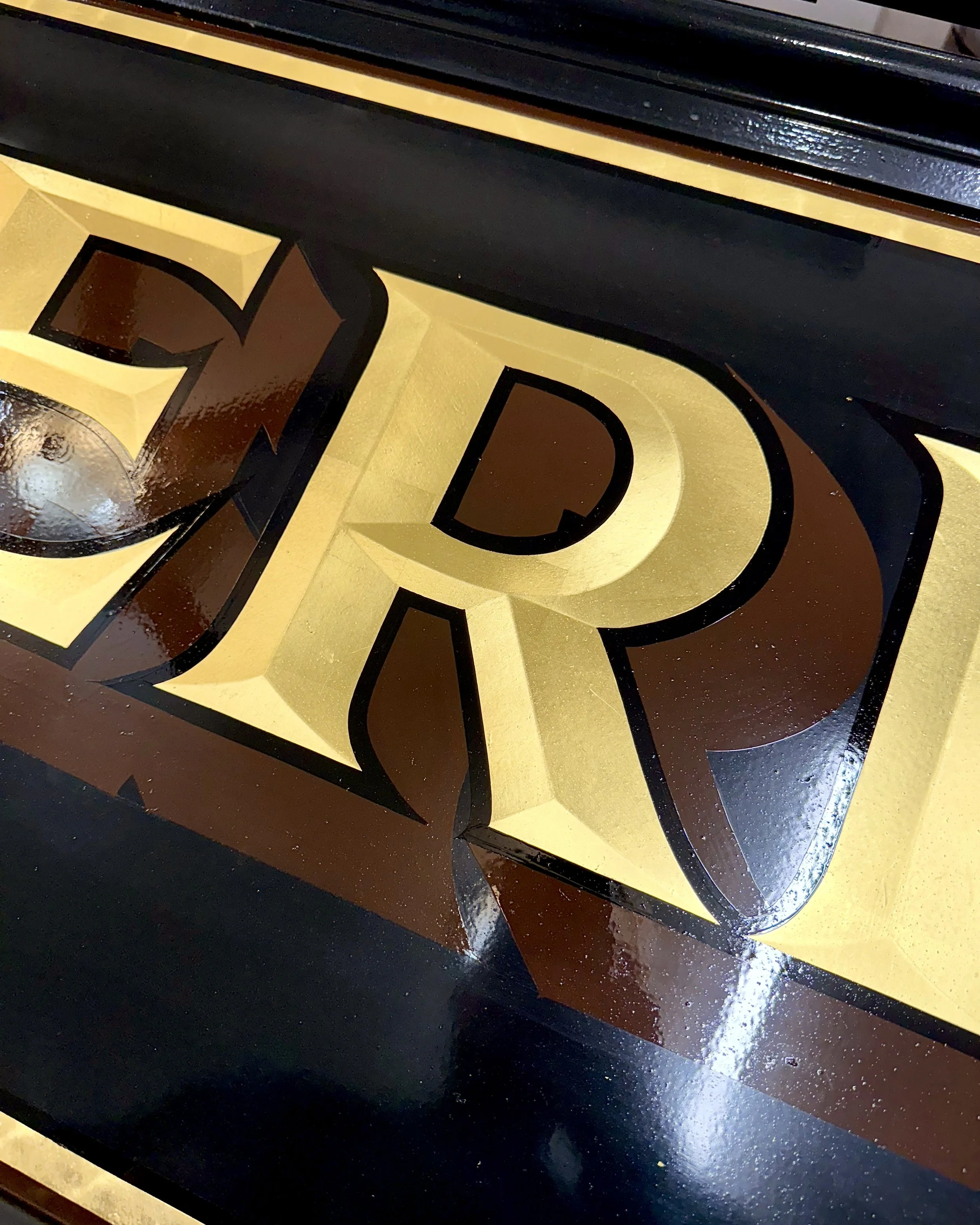 Surface gild detail of a convex-style R in 23k gold leaf.