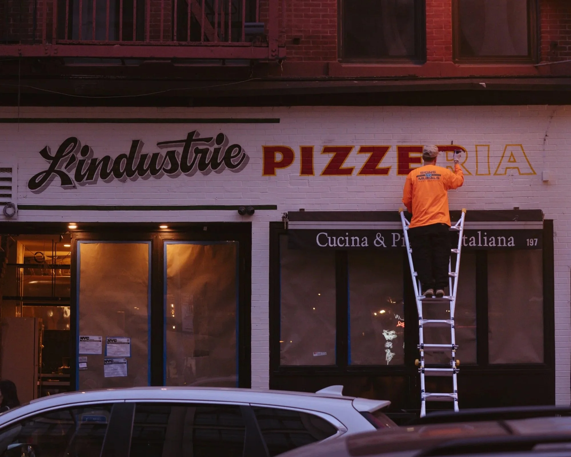 Hand painted sign on brick wall facade for L'industrie Pizzeria's storefront in Little Italy, NY
