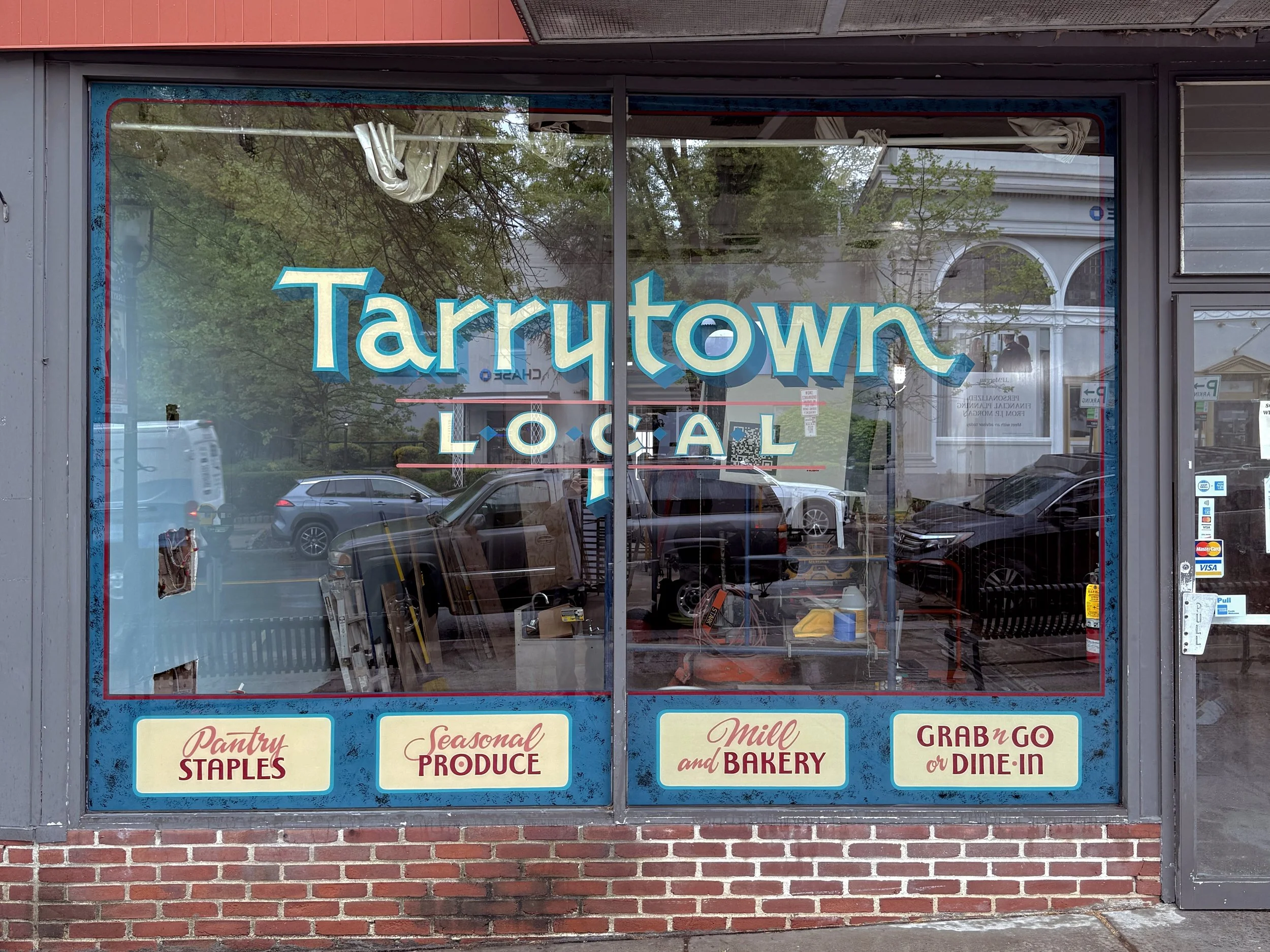 Hand painted sign on storefront windows for Tarrytown Local with logo and border panels.