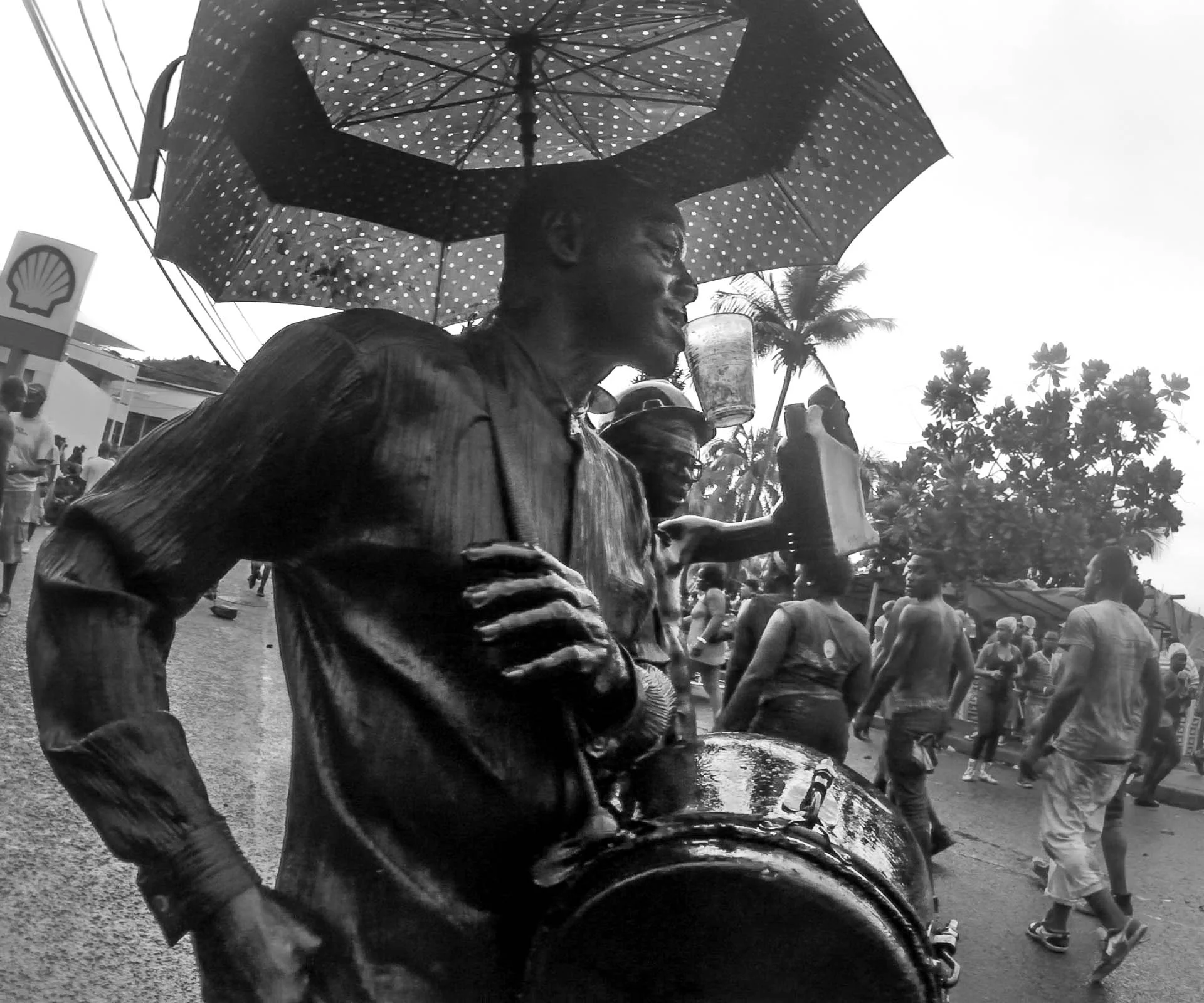 Trucks and floats, laden with speakers, drive slowly down the street as bass heavy music pounds through the crowds. Some players still dance to their own drumming - Video Still, Tom Miller