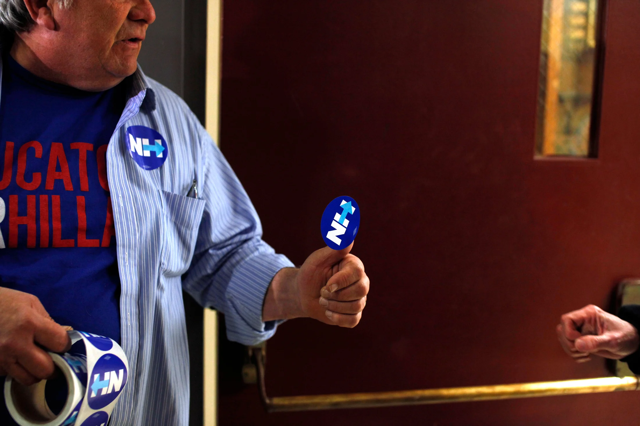 James Mills (L) a volunteer for Democratic presidential candidate Hillary Clinton, hands out stickers before a Get Out The Vote rally at Alvirne High School in Hudson, New Hampshire on February 8, 2016. The event is Hillary Clinton's final pitch to potential voters before the New Hampshire Primary on Tuesday.