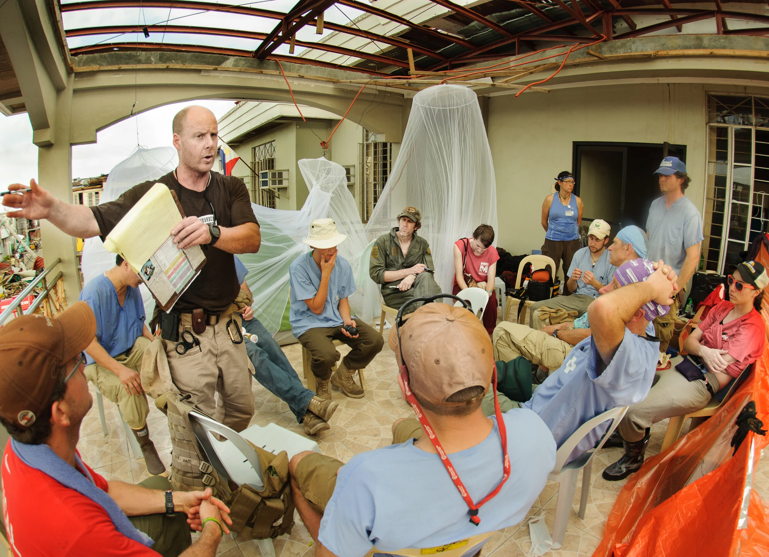 Following a sleepless night cleaning out the town hall, the team listens as Dr. Mike Karch discusses the plan for the clinic's 1st day of operation.