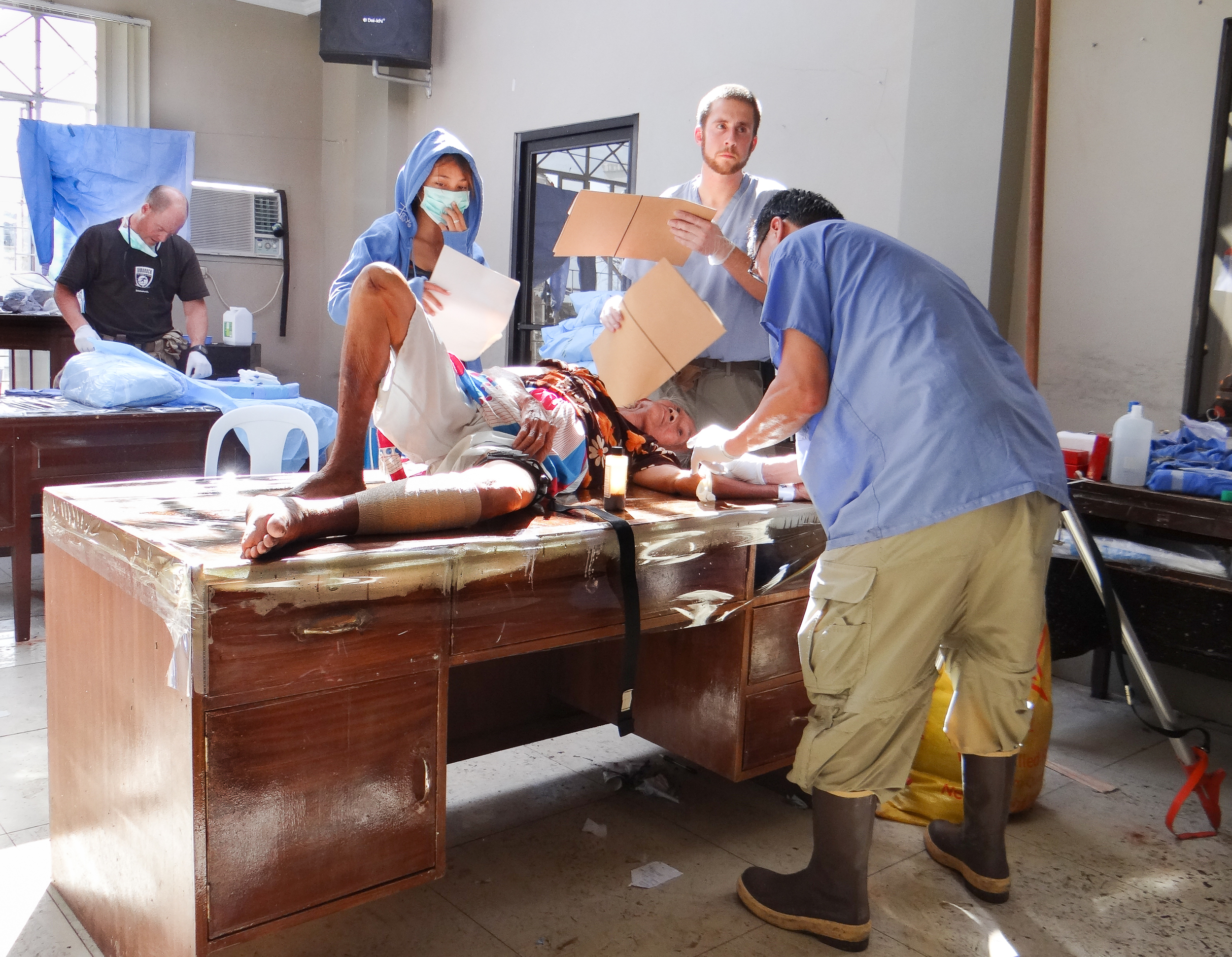 Following surgical treatment of a lower leg wound, a patient's head is shaded from the sun while her IV is removed. 