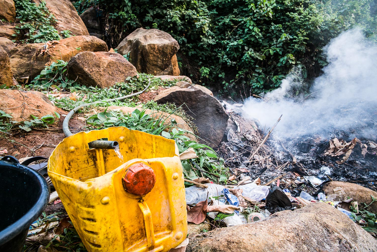 April 2017. In the intervening months since 2015, a neighborhood dump has materialized at the stream's edge behind the Gbakie home. Here, the plastic hoses placed by Francis and his grandmother Nidia slowly fill the family's water container.