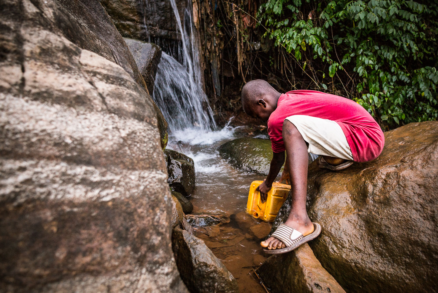 November 2015. In the pre-dawn hour, Francis fetches water from the stream behind the family's home. This will be used throughout the day for bathing, boiling rice, washing dishes and clothes, and drinking water.