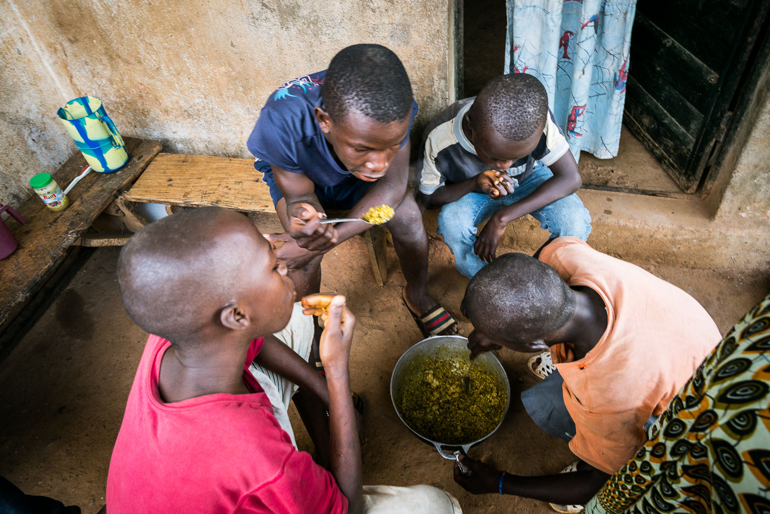 November 2015. Francis and his 3 cousins Earnest, Wilfred, and Michael eat breakfast before school on the front porch of their home. This is more often than not their only meal of the day.