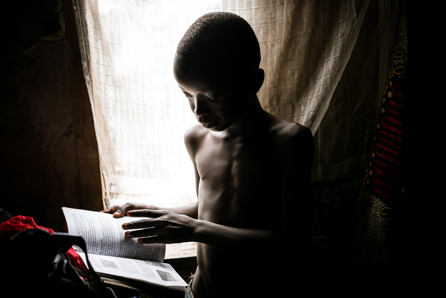 November 2015. Michael Gbakie. Michael, Eye and Matthew's youngest son, pores over a school textbook belonging to his older brother in his parents' room, the only room in the home with a window, and thus the only source of light for homework during