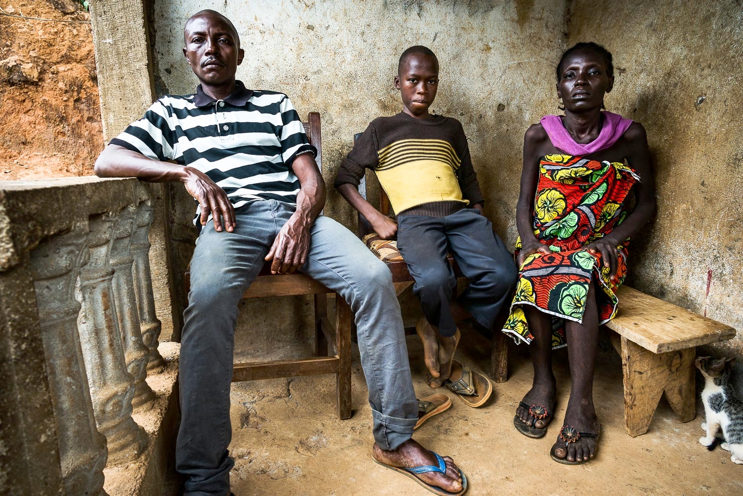 April 2017. A portrait of Francis with his uncle Matthew and aunt Eye in front of their home. Eye is gravely ill with an unknown illness, according to Matthew. The family doesn't have the money to pay for her definitive care. Nonetheless, her sporad