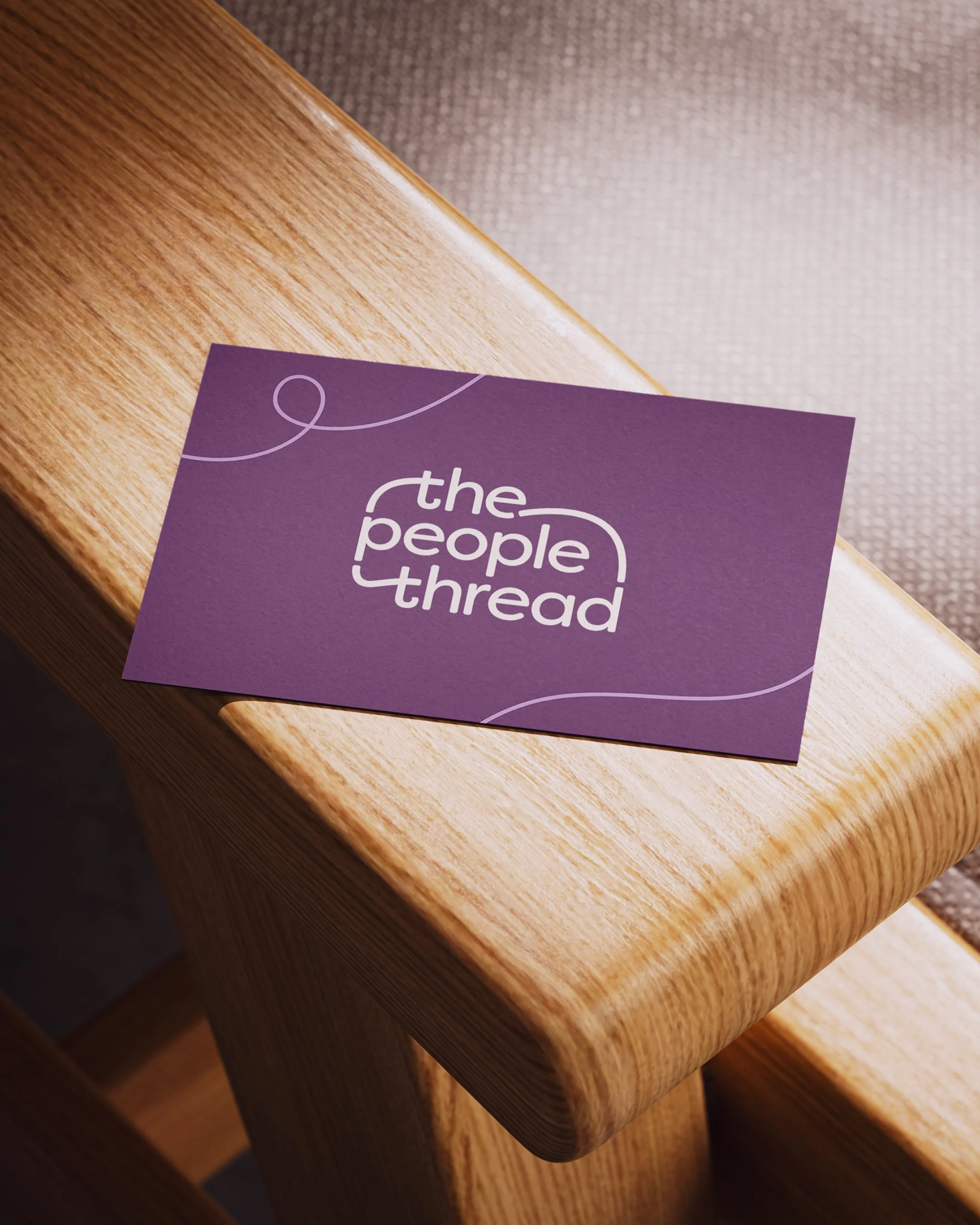 A purple business card with white text reading 'the people thread' resting on the armrest of a wooden chair.