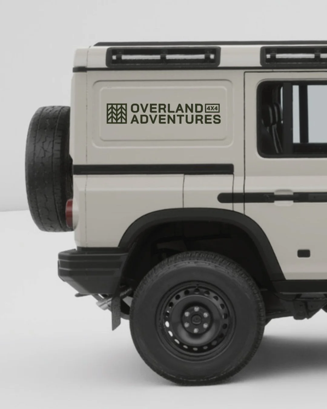 Close-up of the back part of a white off-road vehicle with a spare tire mounted on the rear. The vehicle has a logo that reads 'Overland Adventures 4x4' in green.
