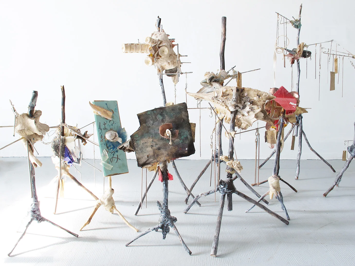 A Series of Three-Legged Idol (2013-2019) sizes vary between 8"~15" in height, found tree branch, sea shell, animal bone, peeled bark and aluminumpigment, copper, brass and origami