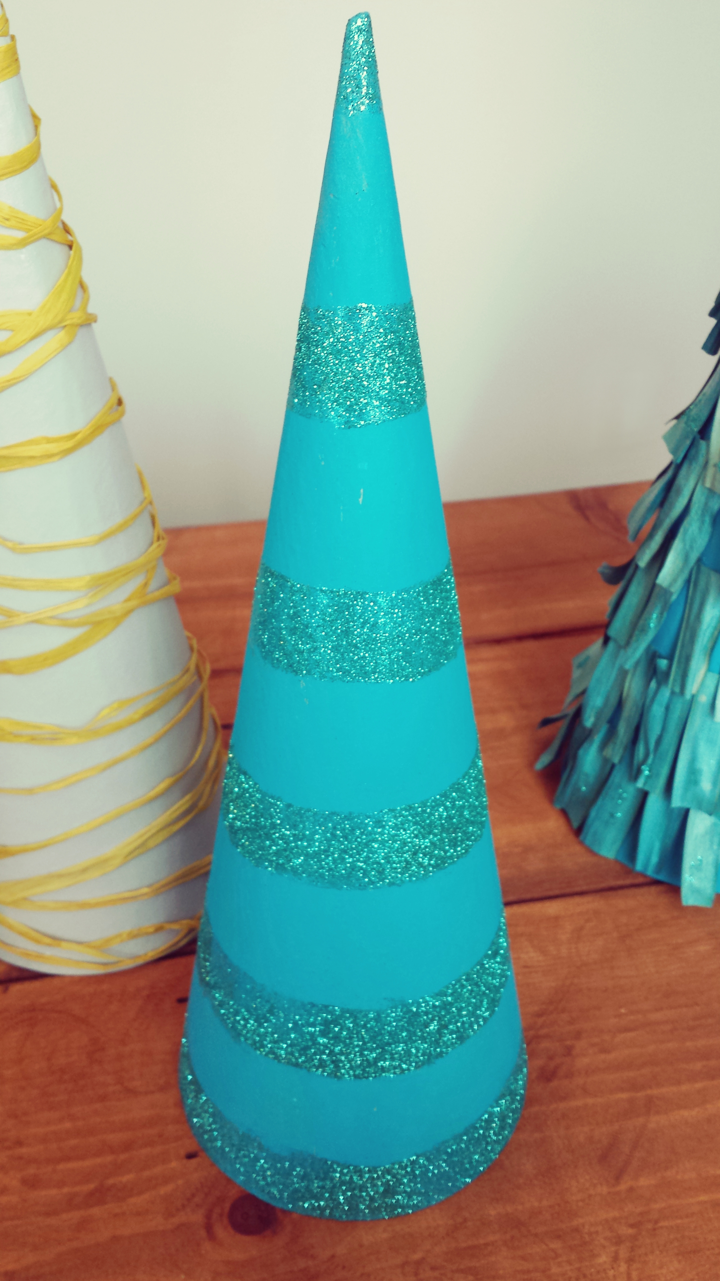 For the glitter tree I simply painted it with the acrylic paint with a cheap foam brush and let it dry. You don't need a lot of paint so it will dry fast. Then I use another foam brush and applied glued on the areas I wanted my stripes. I winged this one but if you don't feel comfortable with that simply use a ruler and pencil and mark the circumference in the areas you want it. It doesn't have to be perfect. For the Raffia Tree I took one end of a raffia string and glued it on the bottom then I began to wrap it around and put glue every now and then where needed. 