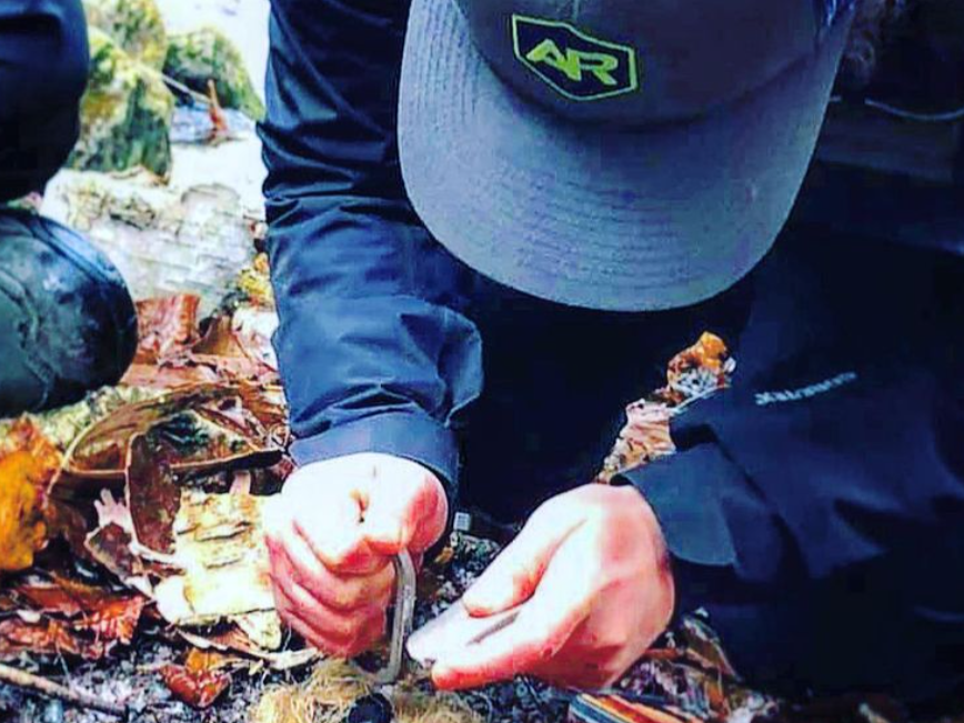Person outdoors using a multi-tool to pry open a shell or a rock surrounded by fallen leaves.