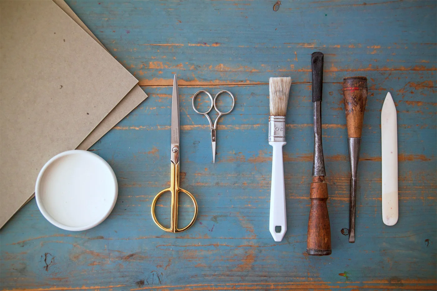 Materials: Rifle Paper Co. Gift Wrap or other fine paper * Studio Carta Tight Weave Ribbons two 8x10 pieces of bookbinding archival board, available at specialty online stores such as: Talas or Hollanders acid-free booking binding glue small brush bone folder, also available at Talas or Hollanders Studio Carta Paper Scissors with Gold Handle Studio Carta Ribbon Scissors hammer ruler X-Acto or utility knife * When considering the entire line of Rifle Paper Gift Wrap and Studio Carta Ribbon, the possibilities are endless. Just let the occasion be your guide. For example, if you're making a book for the parents of a baby boy, perhaps you could use Rifle Paper Co.'s Blue Toile Gift Wrap with Studio Carta Tight Weave Ribbon in Chartreuse . Or for a wedding Rifle's Spearmint Blossoms Gift Wrap would look smashing with a bit of Studio Carta Metallic Tight Weave in Natural with Gold Stripe . (See even more colorful combinations on Rifle Paper Co.'s site .) For our book, Justine and I selected spring-time pairing of Rifle Paper Co.'s romantic wildflower gift wrap with Studio Carta Tight Weave Cotton Ribbon in Peach .