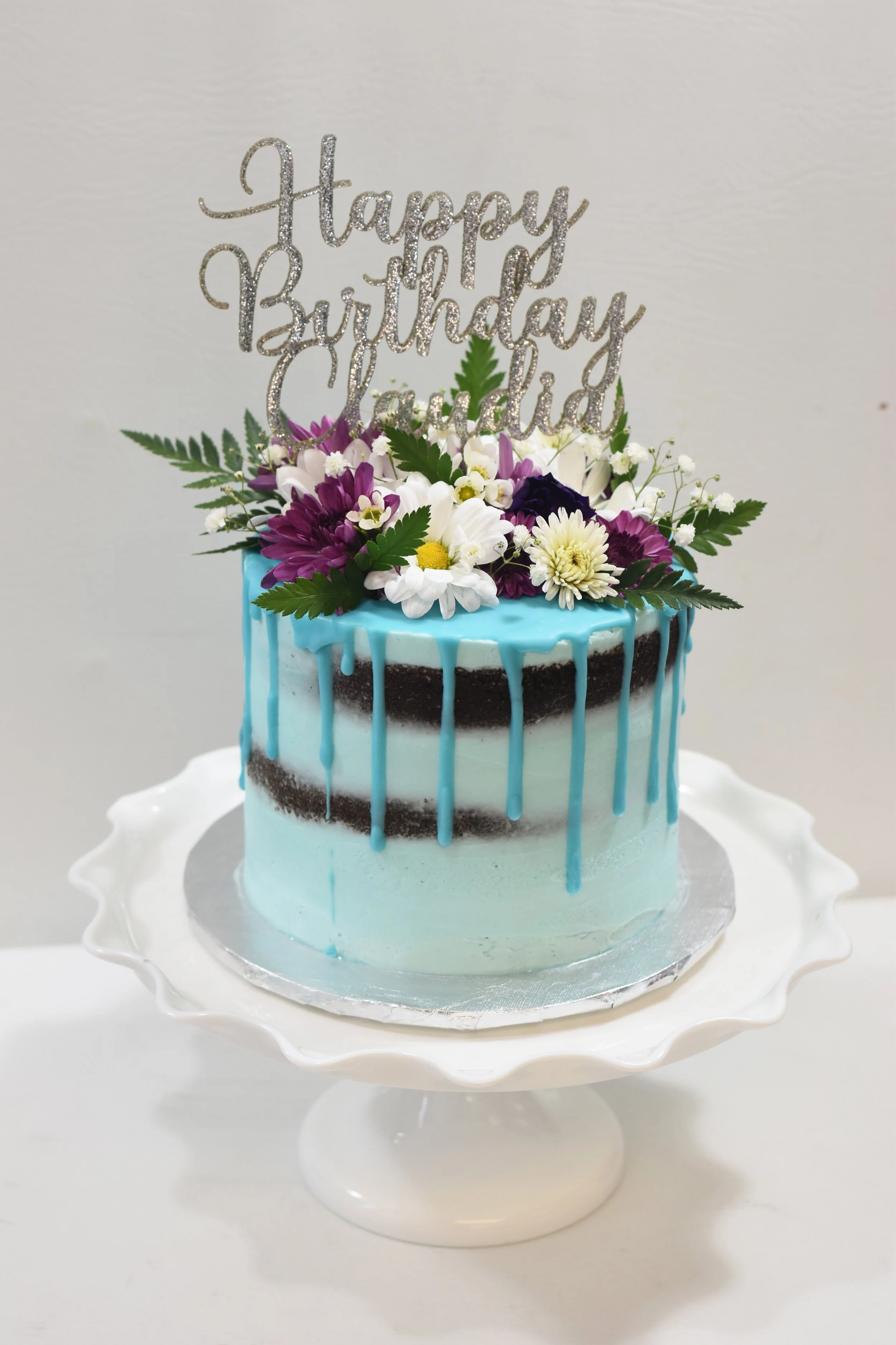 baby blue drip cake with florals and acrylic topper.jpg