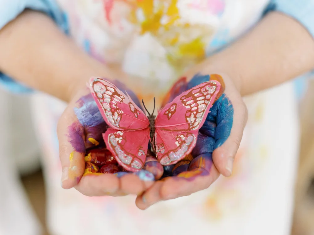 Paint-covered hands cradling a pink paper butterfly