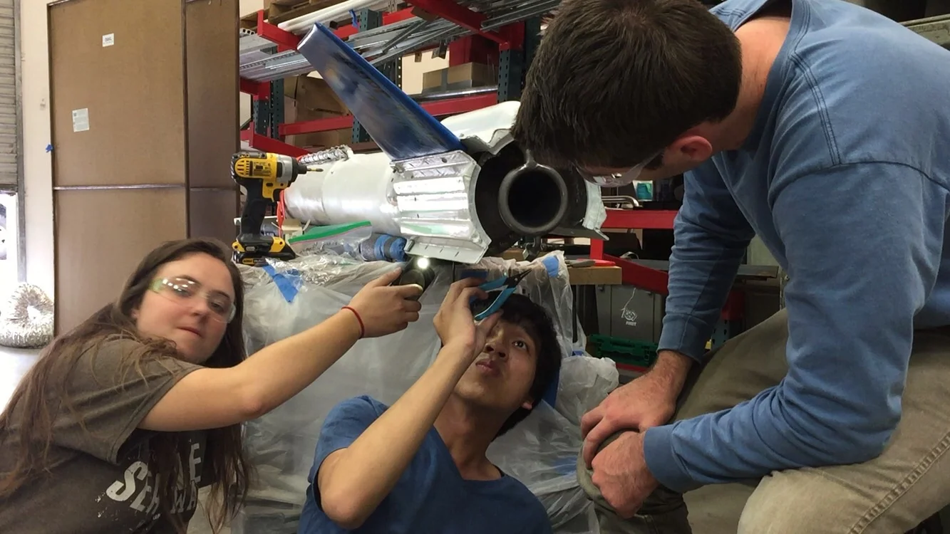 Nikolai Dorbritz, Kevin Hoo, and Zoe Warp work on the integration between the fins, boattail, and engine thrust struts.