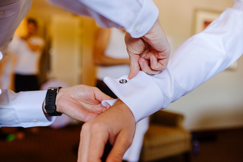 Groomsman helping groom get dressed before wedding