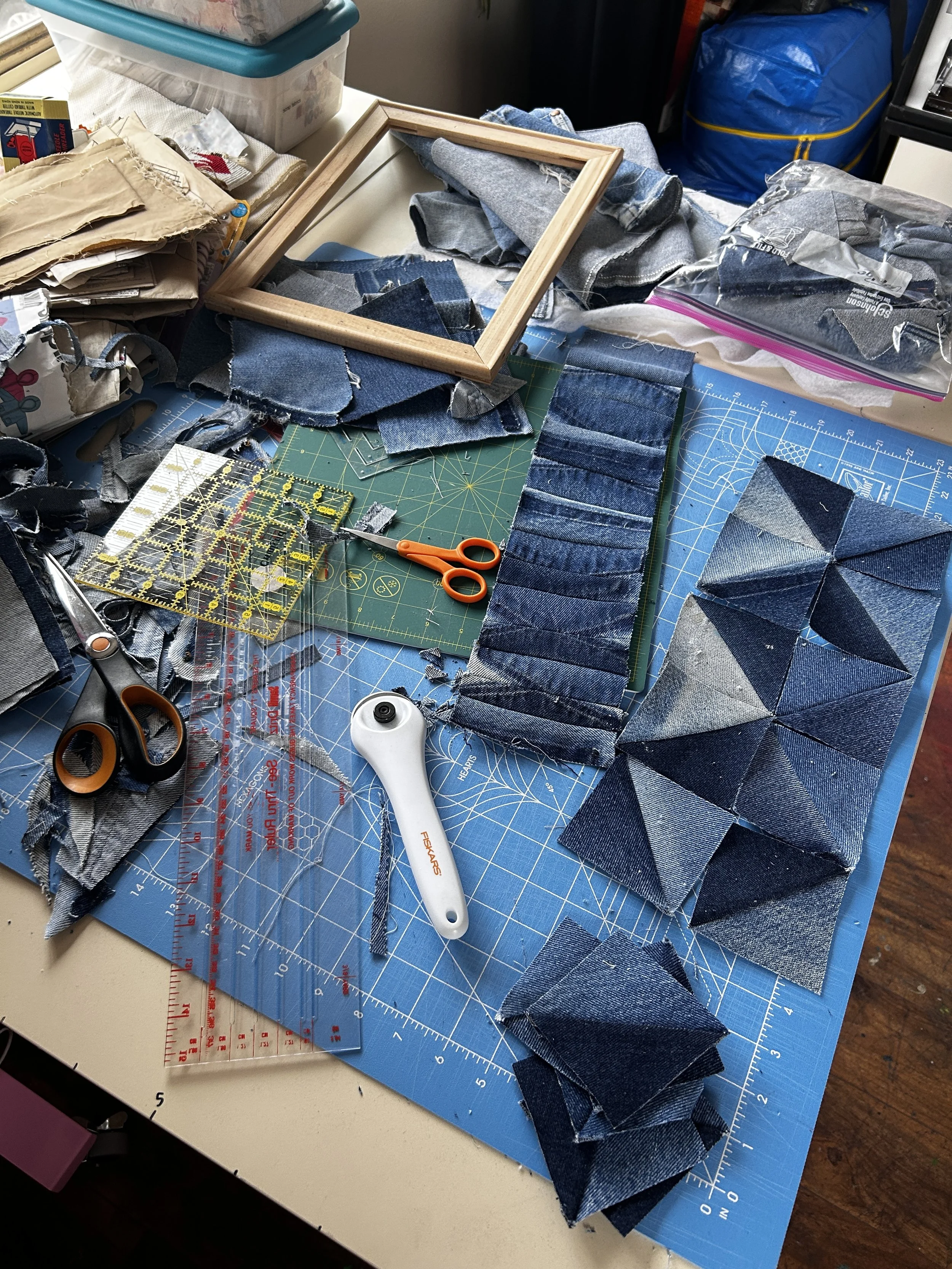 in process shot of a table with denim quilt blocks laid out along with other quilting supplies