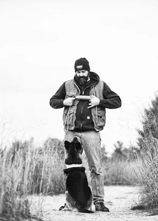 Dan Dudley holding a toy with German Shepherd, Gretta, sitting in front of him.