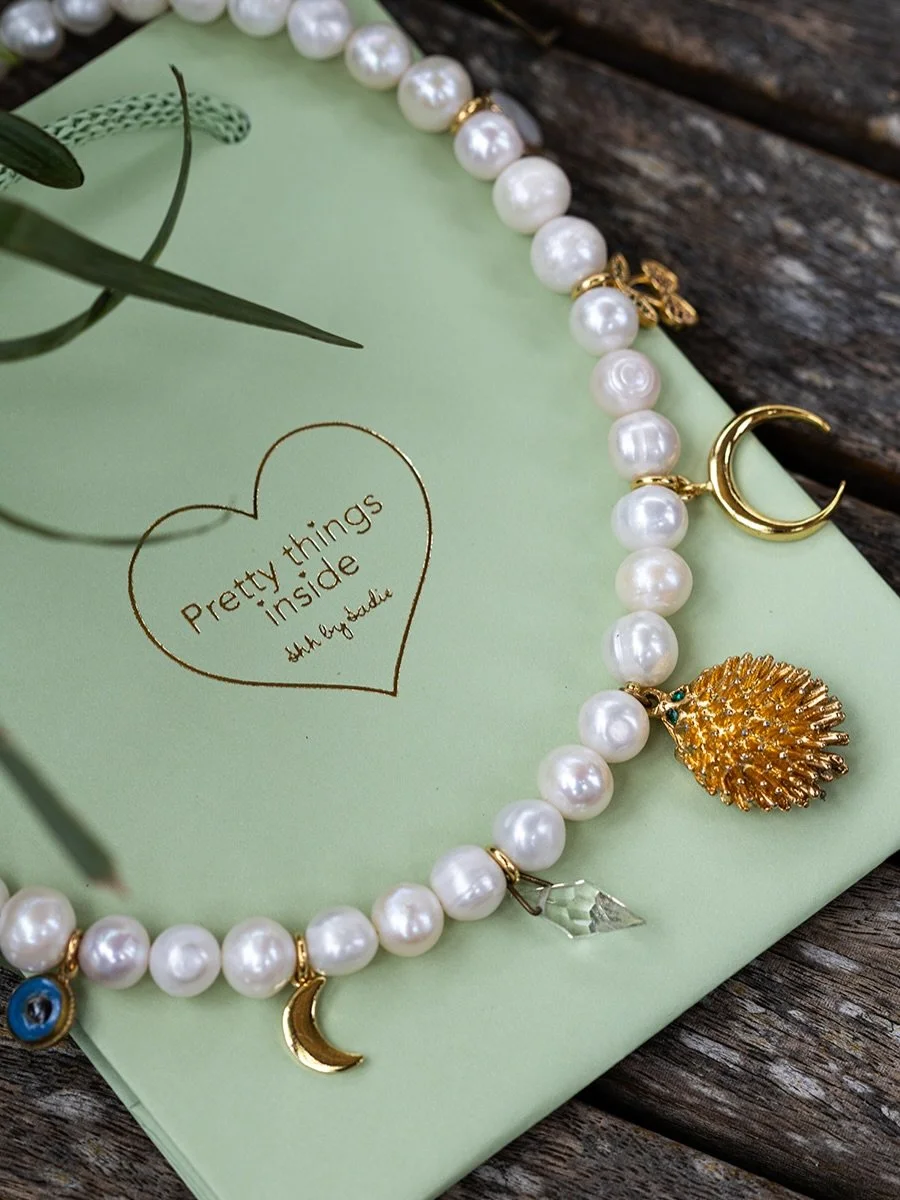 A one-of-a-kind mix of vintage charms and chunky, shimmering freshwater pearls ✨

Handmade with a collection of vintage charms including  an antique glass evil eye, shiny gold moons, a super cute hedgehog with green diamante eyes, a diamante cherry, 