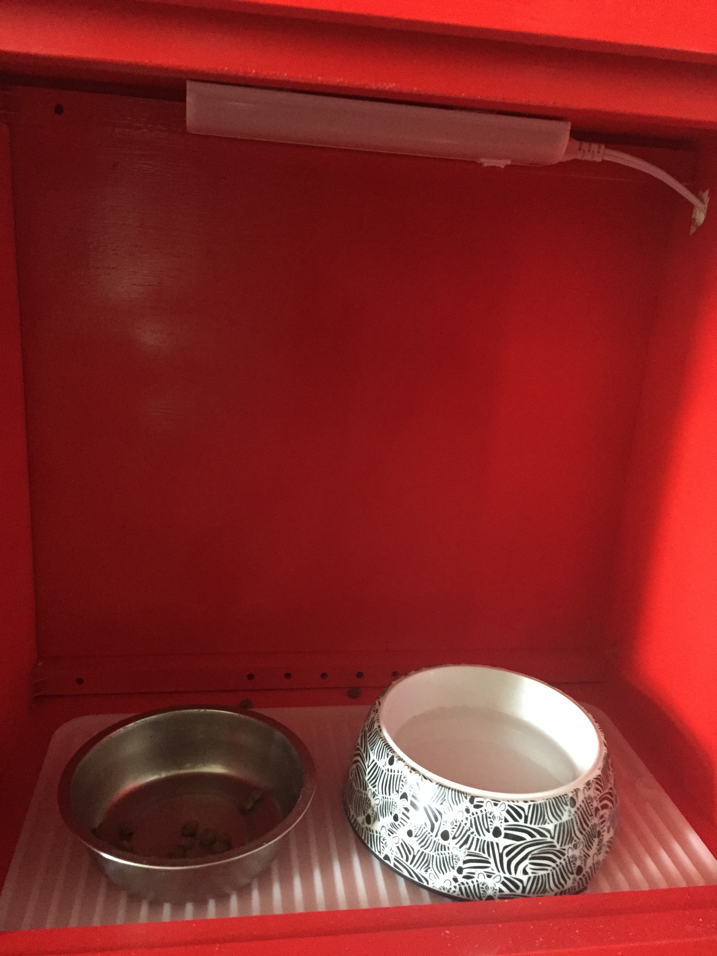 After the paint was dry, I found an under the cabinet light and attached it with double-sided tape to Beasley's food area. I drilled a small hole into the side of the cabinet to wire the cord through it. Next, I added a silicone drying mat to place her bowls on. 