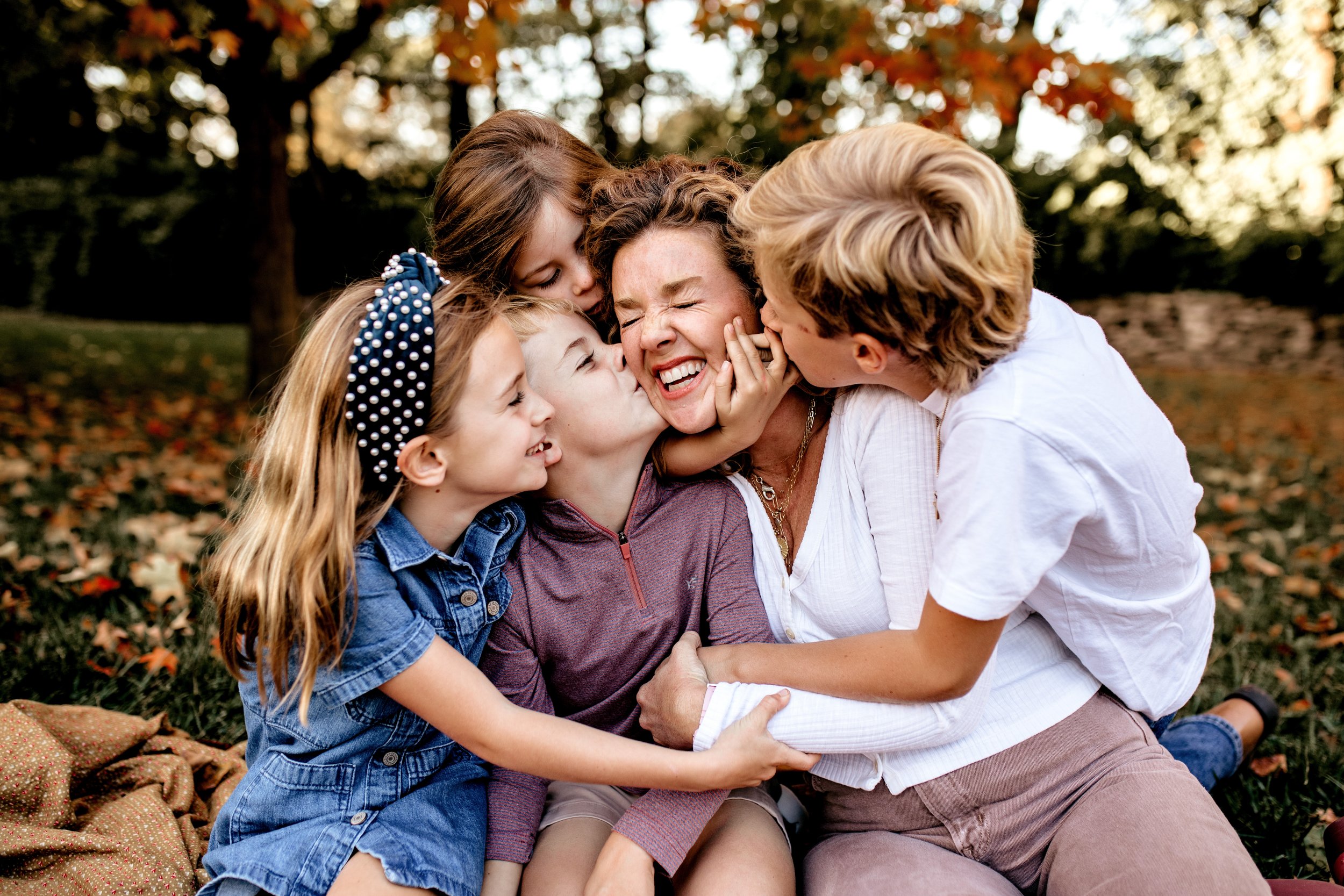 A woman and four children are outdoors in a park during autumn, smiling and hugging each other tightly.   Lifestyle outdoor family session in Nashville, TN