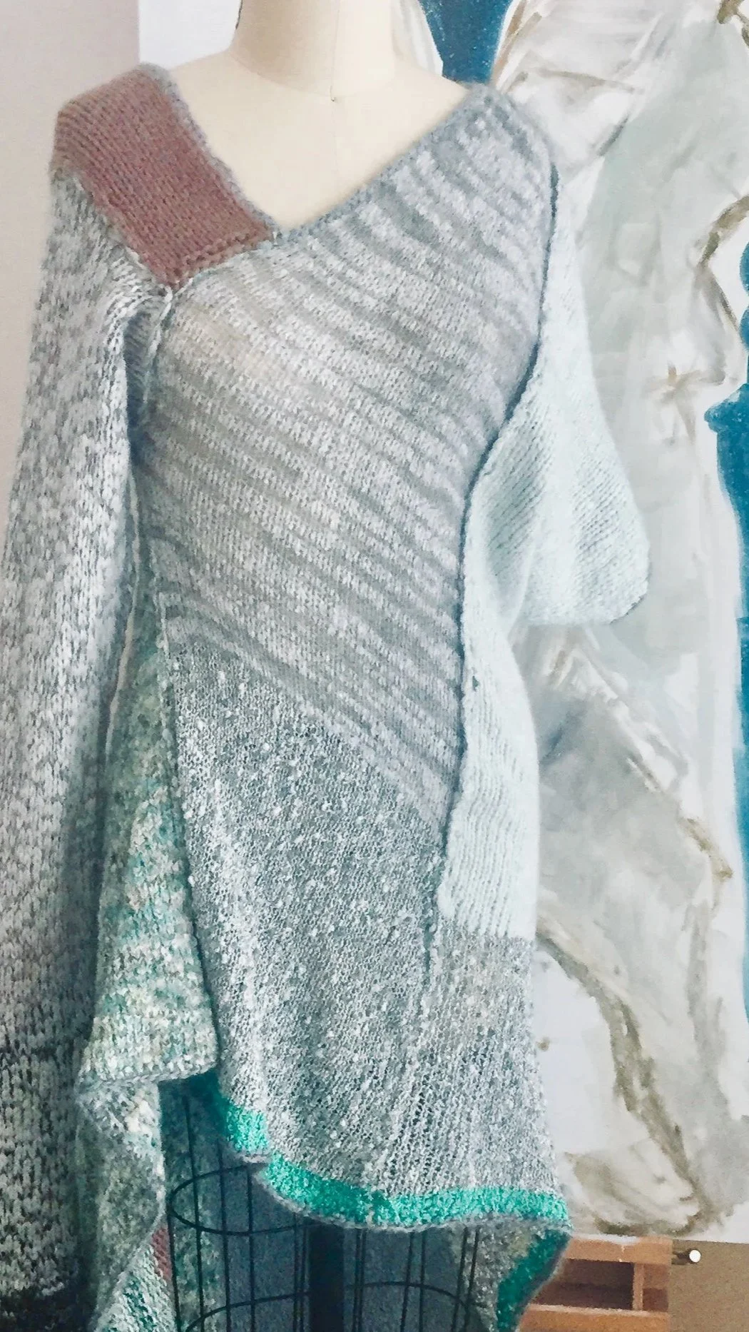 Colorful knitted sweater displayed on a mannequin with an abstract painting in the background.