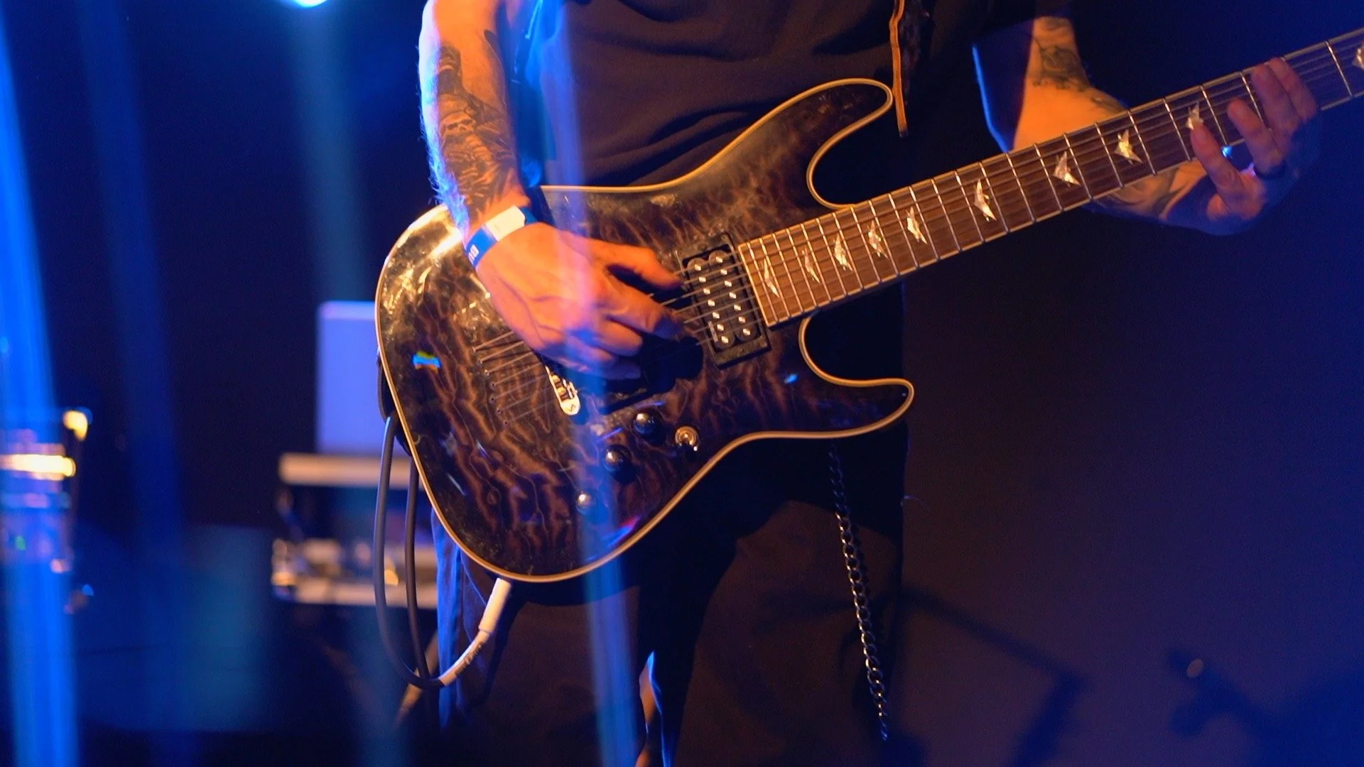 Guitarist performing on stage with electric guitar and tattoos under blue stage lights.