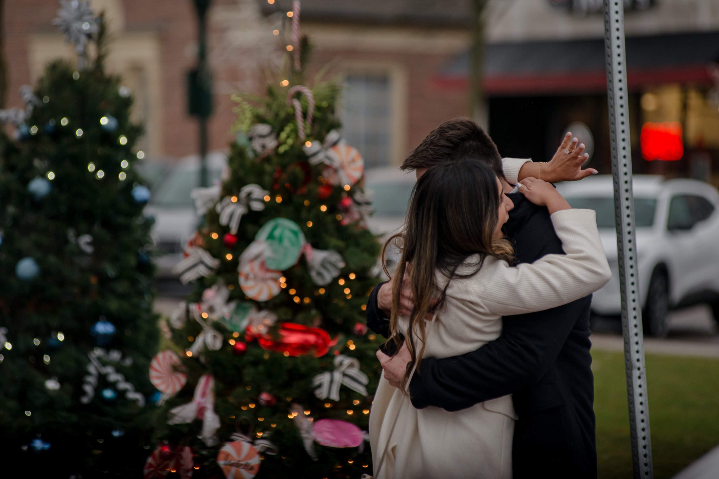 Downtown Plymouth Michigan proposal with bride looking at engagement ring while hugging fiancé