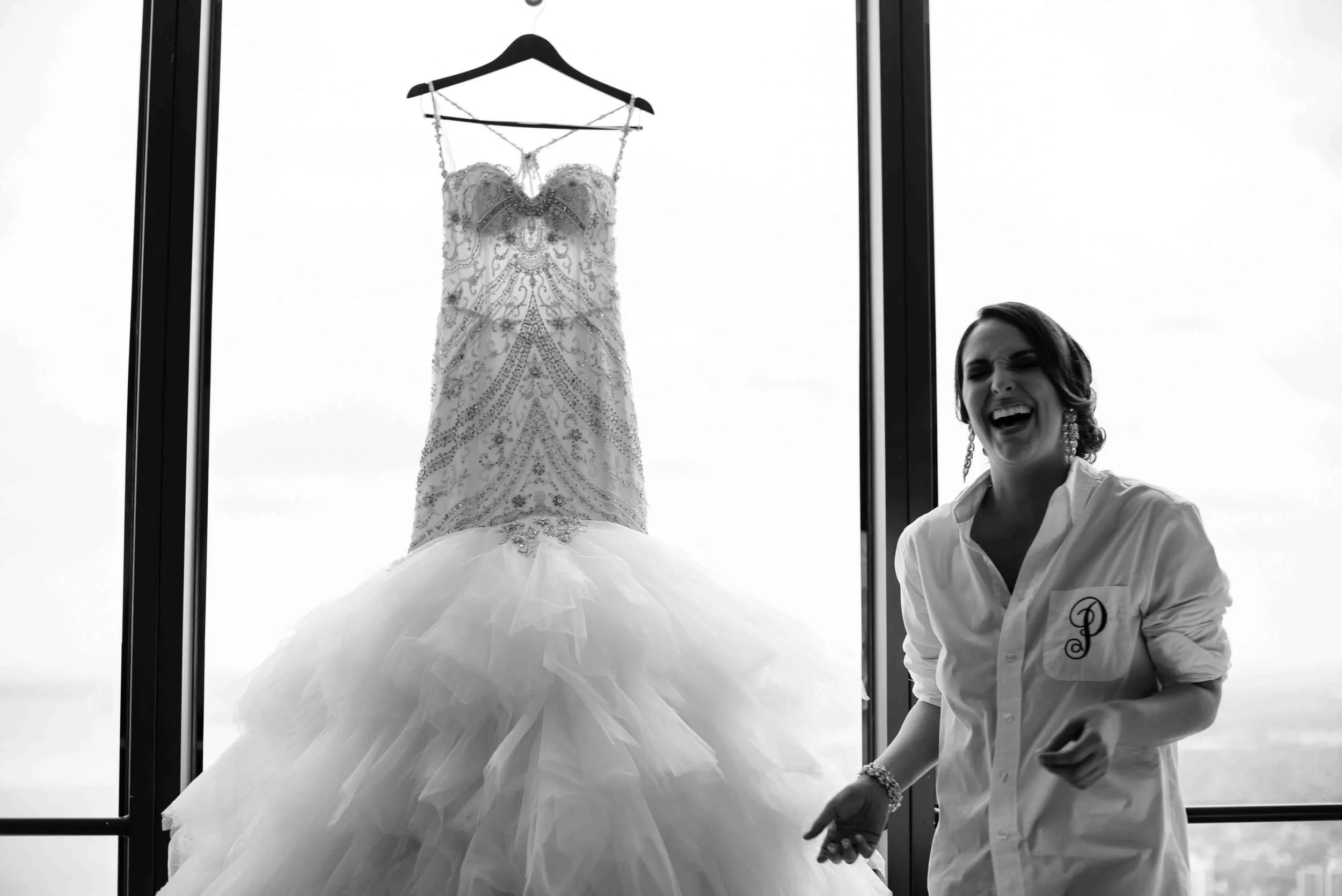 Bride laughing joyfully with her wedding dress hanging