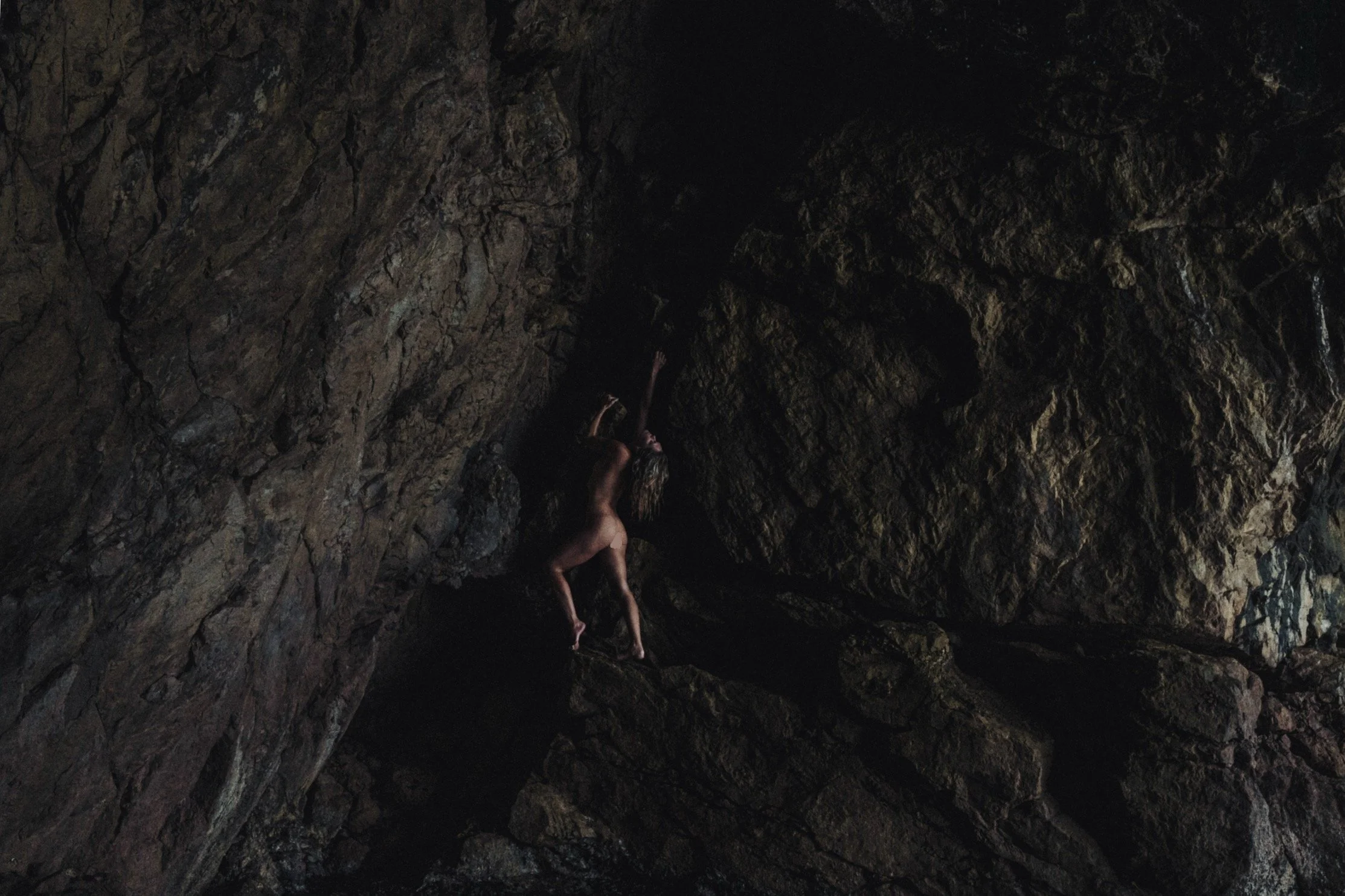 A person appears to be climbing or hanging on the rocky interior of a dark cave.