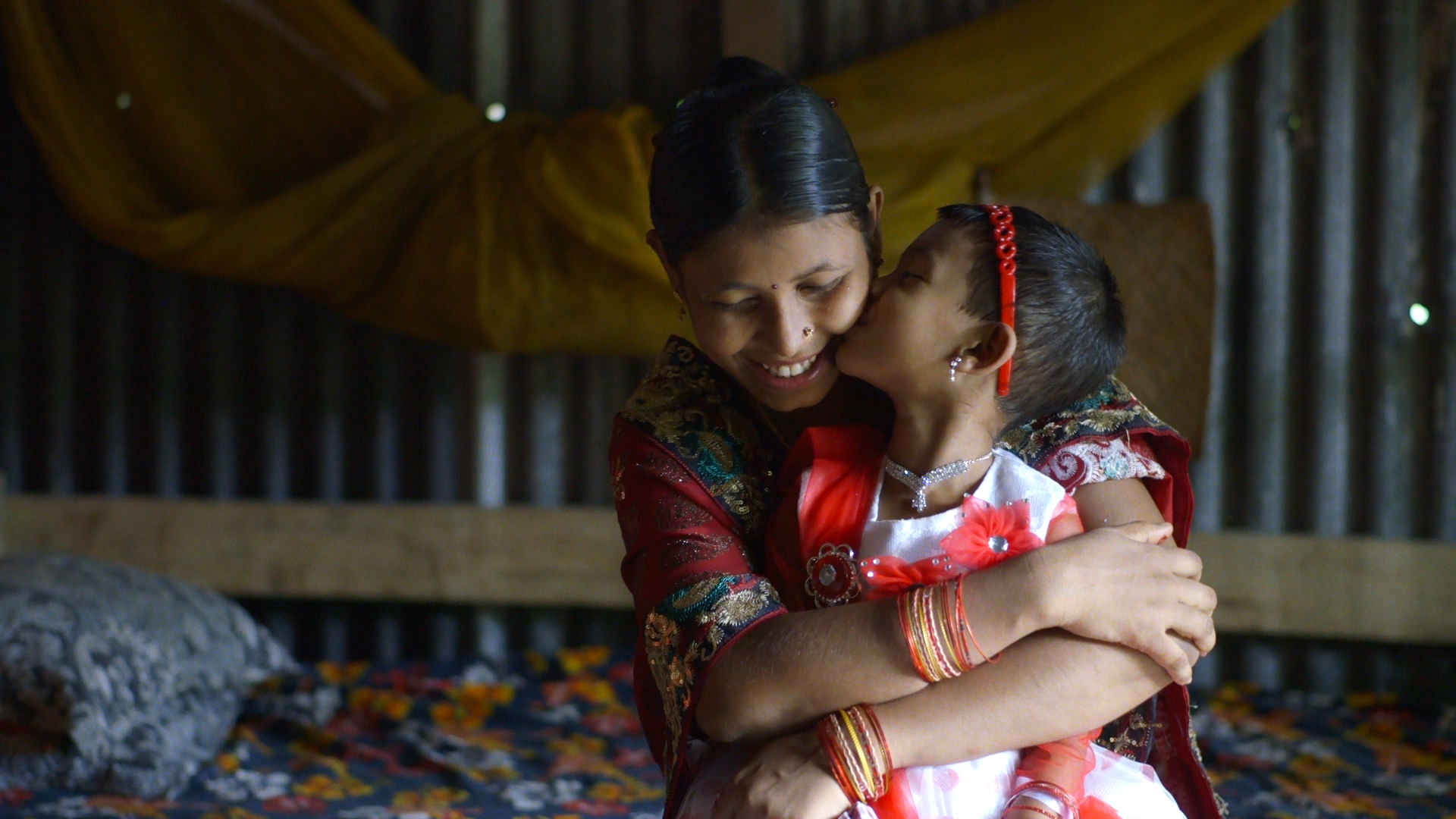 Shima Akhter hugs her daughter, Nadia, on the morning that she has to leave her with her family in a village in the countryside. She will only see her twice a year, since Shima must remain in Dhaka to work at a garment factory. Image Source: The True Cost.