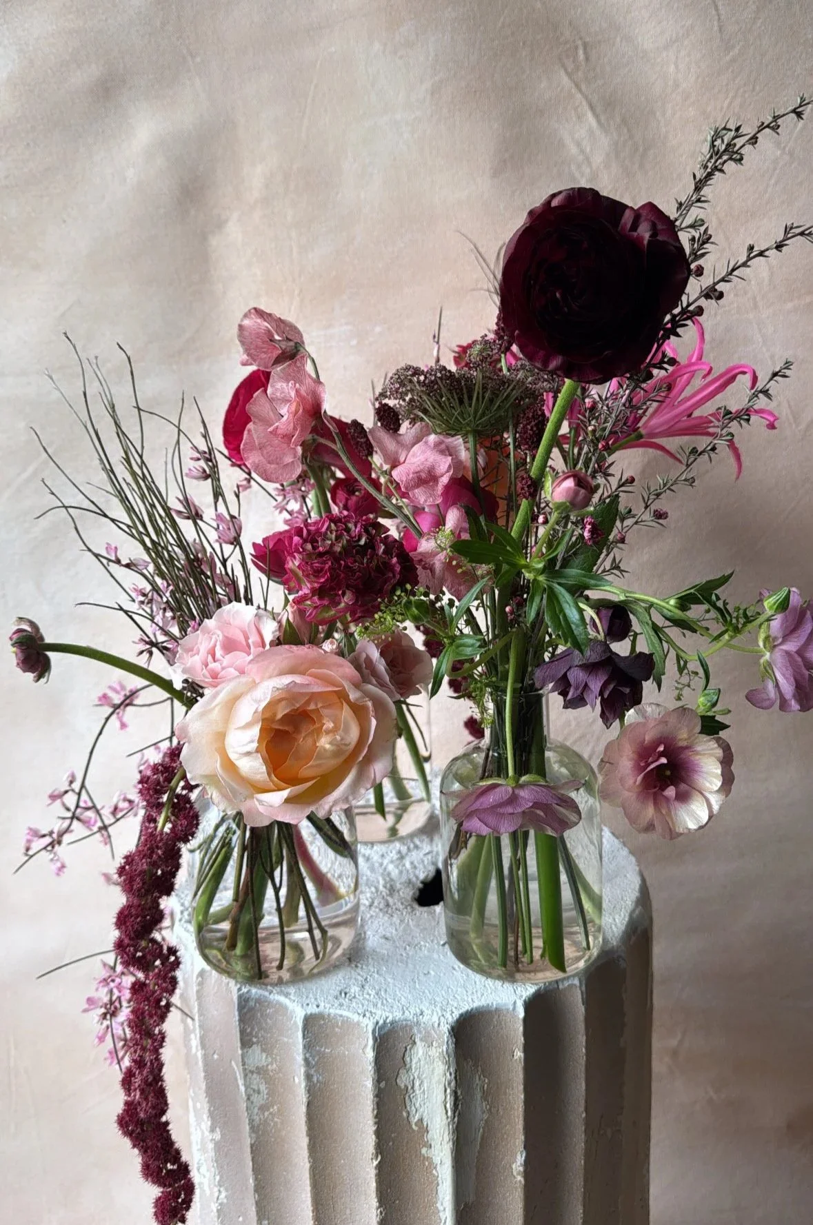 A trio of glass bud vases with florals in a moody color palette