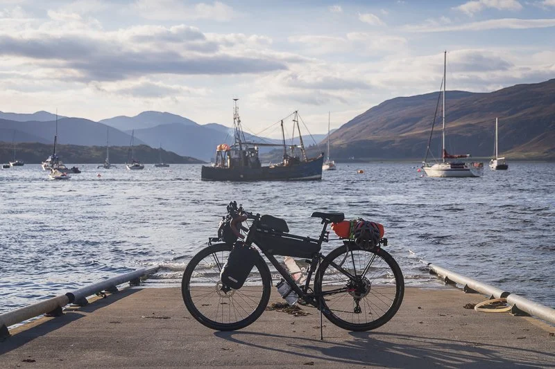A Bikepackers bike setup in front of a seascape scene in Scotland