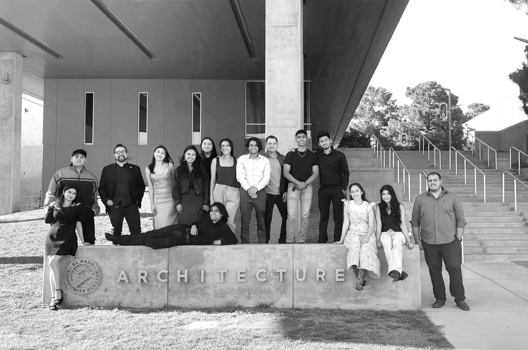 Group of university students posing in front of a modern building and a sign that reads 'ARCHITECTURE'.