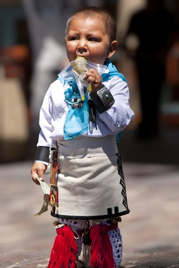 Little Native American boy, eating pickle and holding a dollar bill. 