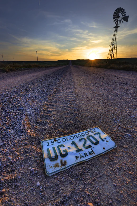 Sun sets over gravel road and windmill. 