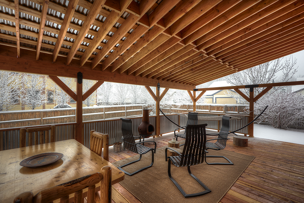 Large, covered wood deck with corrugated steel roof and side-rails custom-built by Gary Foutch, Colorado Custom Trim. Featuring black steel joinery and redwood decking. Log furniture from Cabela's; Homecrest Andover Spring Base outdoor chairs in black; steel arc hammock stand by Hatteras Hammocks; cast iron chiminea by Aussie Heatwave; and, outdoor rug by Plow & Hearth. Cottonwood and beetle kill pine side tables by homeowner. 