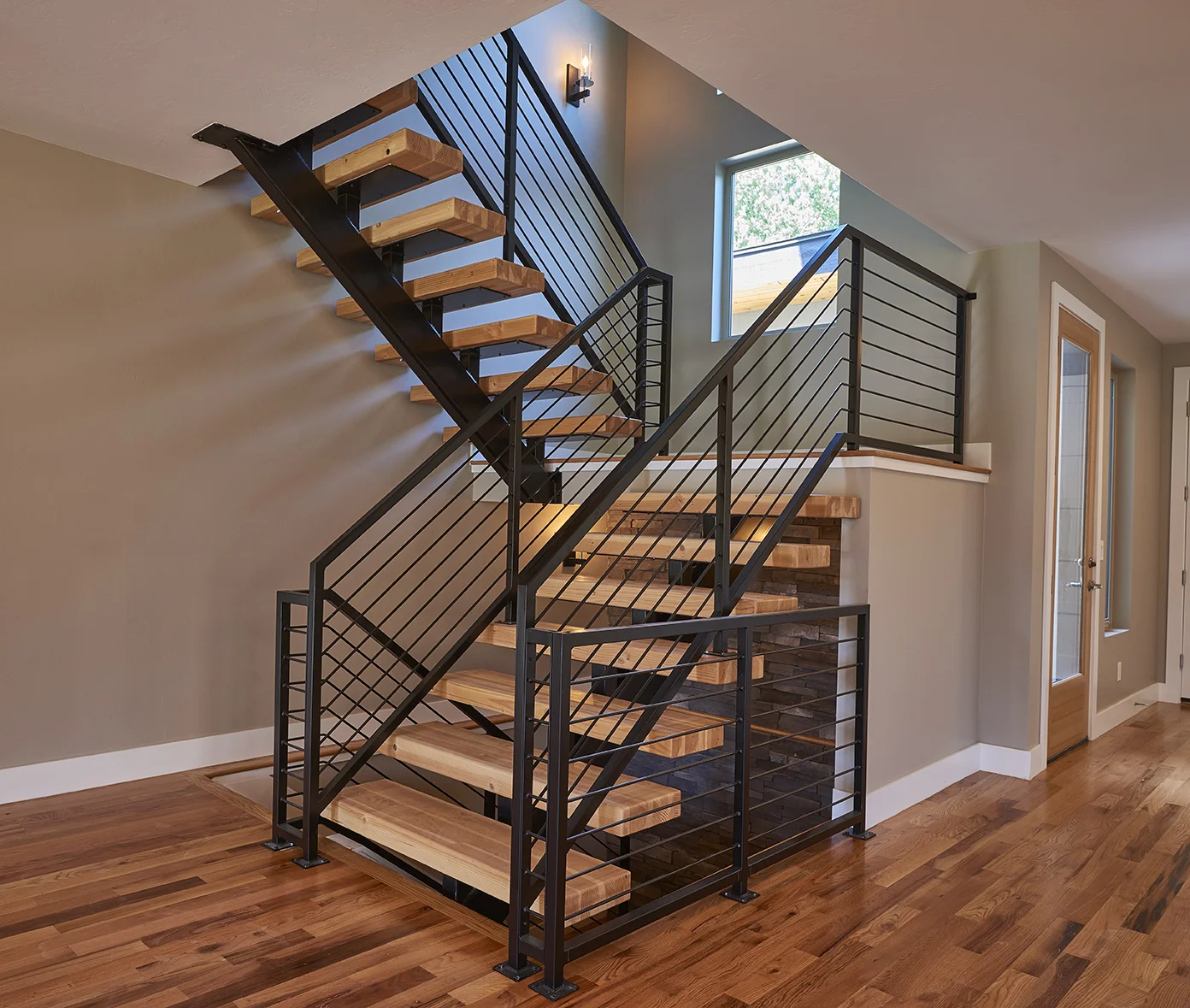 Modern stairwell with black iron handrails and floating butcher block stairs.