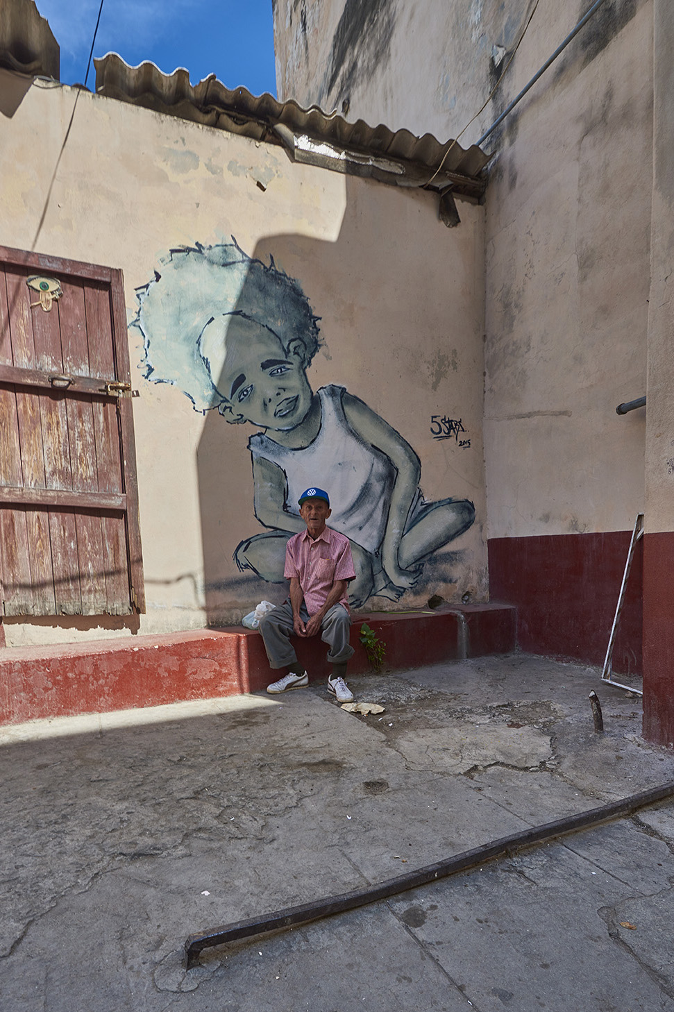 Man sitting on stoop, next to wall mural in Cuba. 