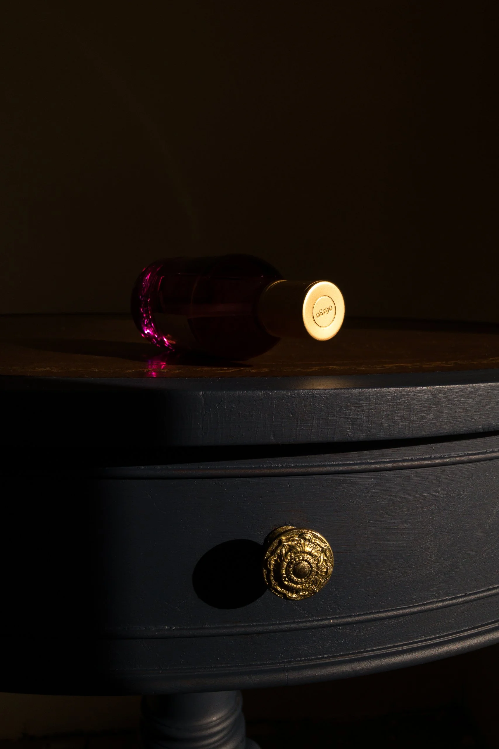 Parfums 06130 Plum crystal perfume flacon with gold cap on dark blue antique table