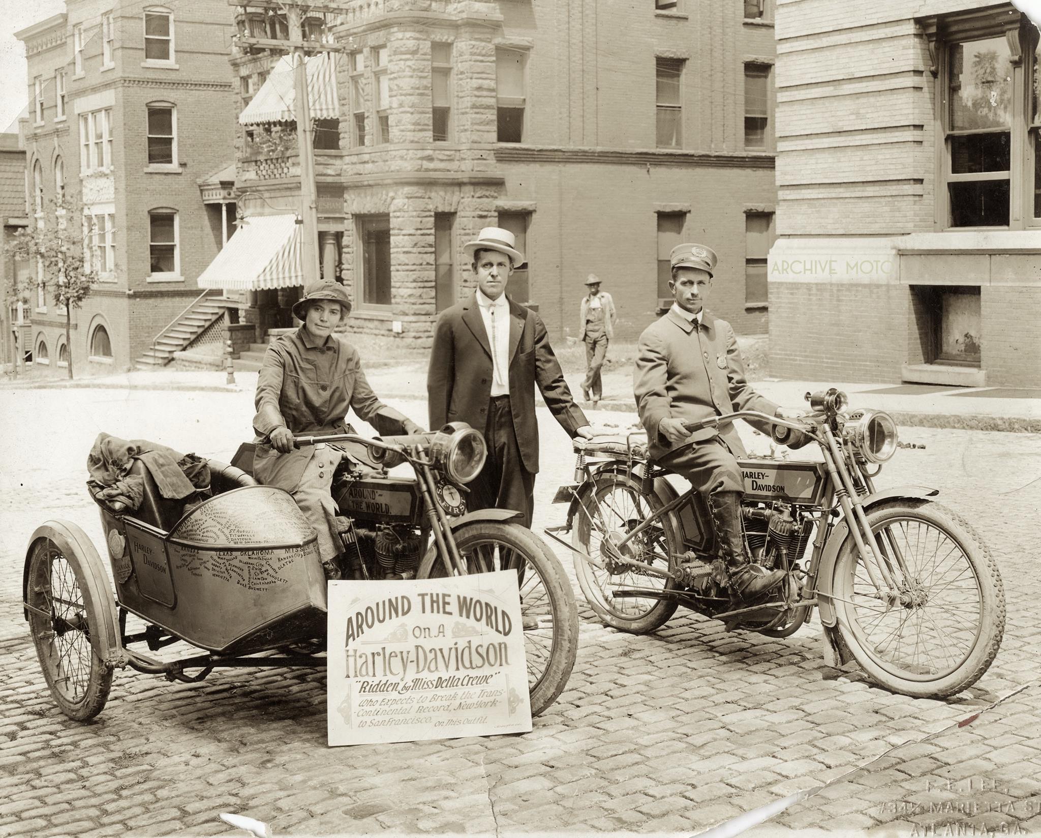 Here is the lovely and rugged Miss Della Crewe on the streets of Atlanta in September, 1915 after having just returned to the US from her continued motorcycling adventures in South American and the Caribbean. She sits atop her 1914 Harley-Davidson sidehack rig adorned with the names of towns and states which she had visited the year before, as well as the plates, plaques, and badges from her recent international trips. After beginning her journey in June the year before, Crewe had traveled over multiple continents, numerous countries, countless states, and had covered nearly 11,000 miles with only the company of her trusty companion Trouble, a feisty little terrier, who is somewhere out of frame assuredly living up to his name. She is accompanied by local Harley-Davidson dealer Gus Castle and an Atlanta Police Officer.