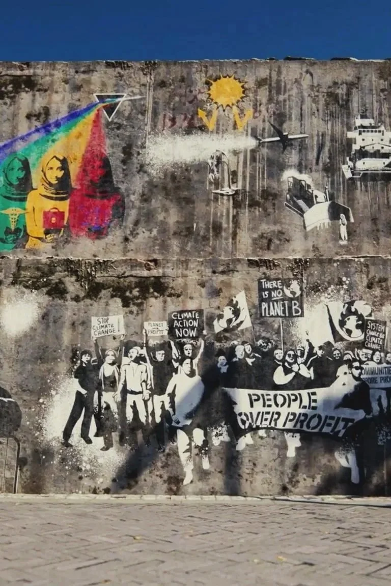 Street mural depicting multiple layers of street art, including colorful portraits, protest signs, and silhouettes of protestors with banners advocating for climate action and social justice.