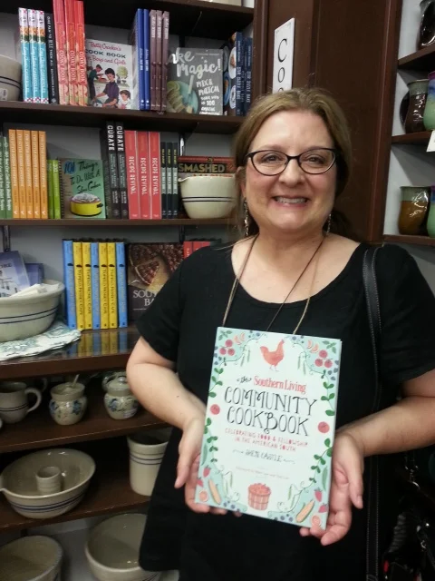 Sheri Castle holding a copy of her cookbook "The Southern Living Community Cookbook, Celebrating Food and Fellowship in the American South".