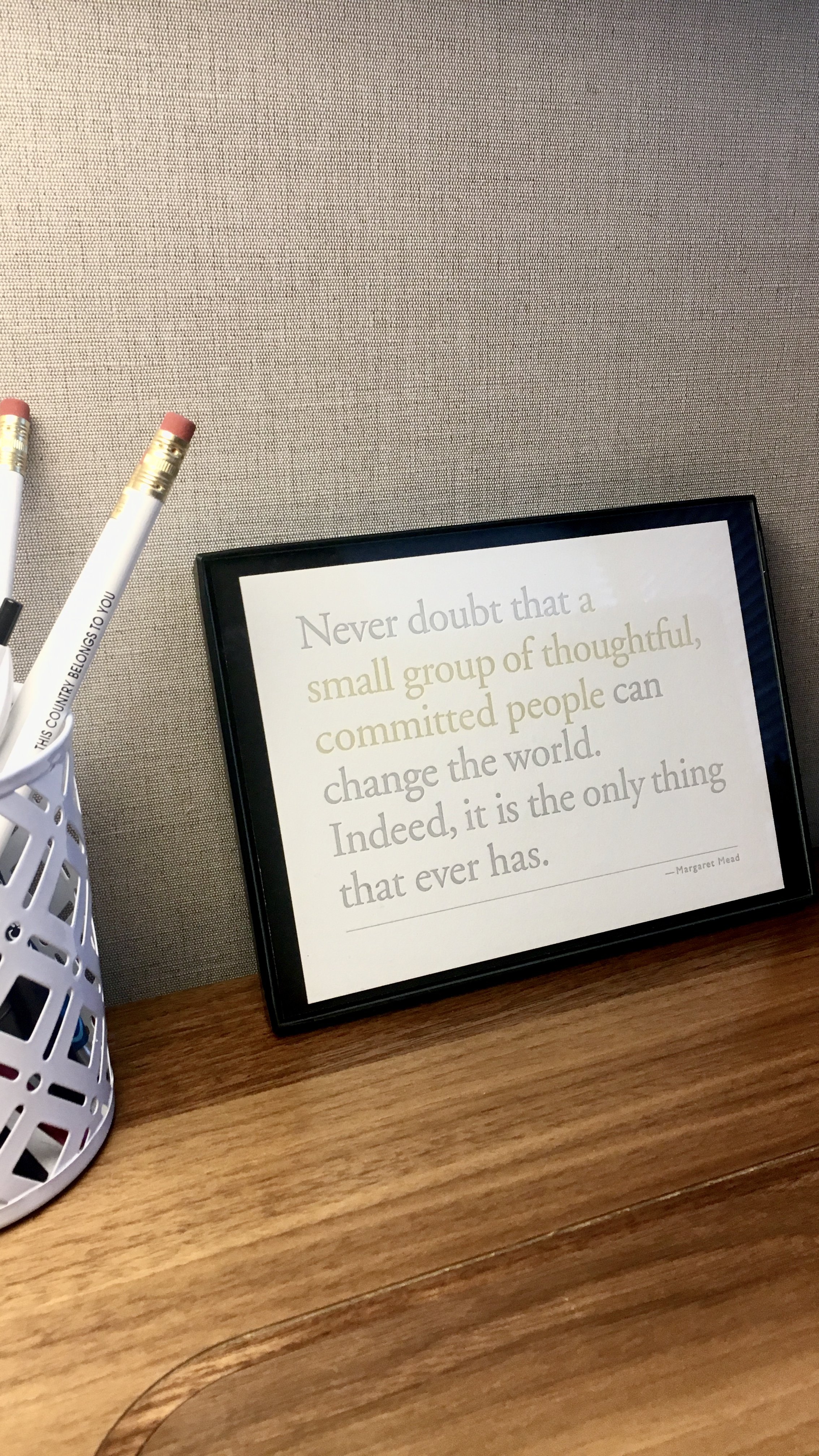 Framed quote on desk with pens. Quote reads: 'Never doubt that a small group of thoughtful, committed people can change the world. Indeed, it is the only thing that ever has. - Margaret Mead.'