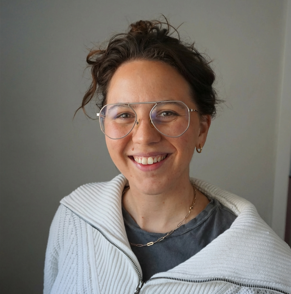 Portrait of Koly, woman with brown hair, glasses, and a white sweater on.